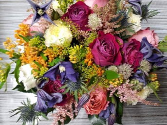 An overhead view of a lush and colorful bouquet of flowers with a rustic, wild aesthetic. The arrangement includes a mix of textures and colors, featuring magenta and pink roses.